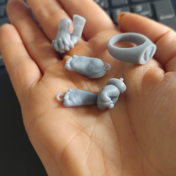 3D geprinte prototypes van 3D geprinte handjes en voetjes in grijze resin liggend op een hand