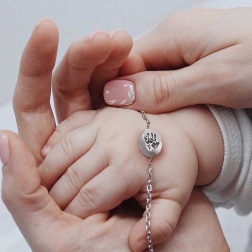 volwassen en babyhandje houden bedel op armbandje vast. geboorte sieraden imprintedme