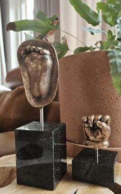 Bronzen handje volledig met een bronzen voetje halve indruk op een zwarte sokkel. Van je kleintje een beeldje laten maken